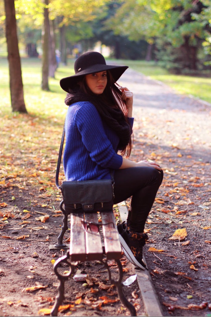 Sylwia w kapeluszu z dużym rondem i niebieskim sweterku pozuje do zdjęcia na ławce w parku