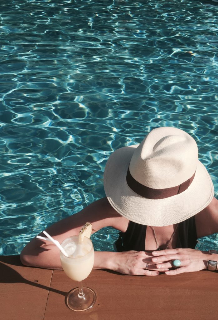 modelka z drinkiem i kapeluszem panama w basenie